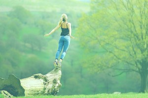 Motivierte, sportliche Frau streckt sich auf einem Baumstamm in der Natur